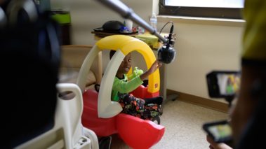 Little boy in hospital in toy car playing with cameraman. Project sunshine behind the scenes film shoot. 5-part promotional campaign to highlight the scope and impact of their work. Pediatric patients. Non profit. Production services.